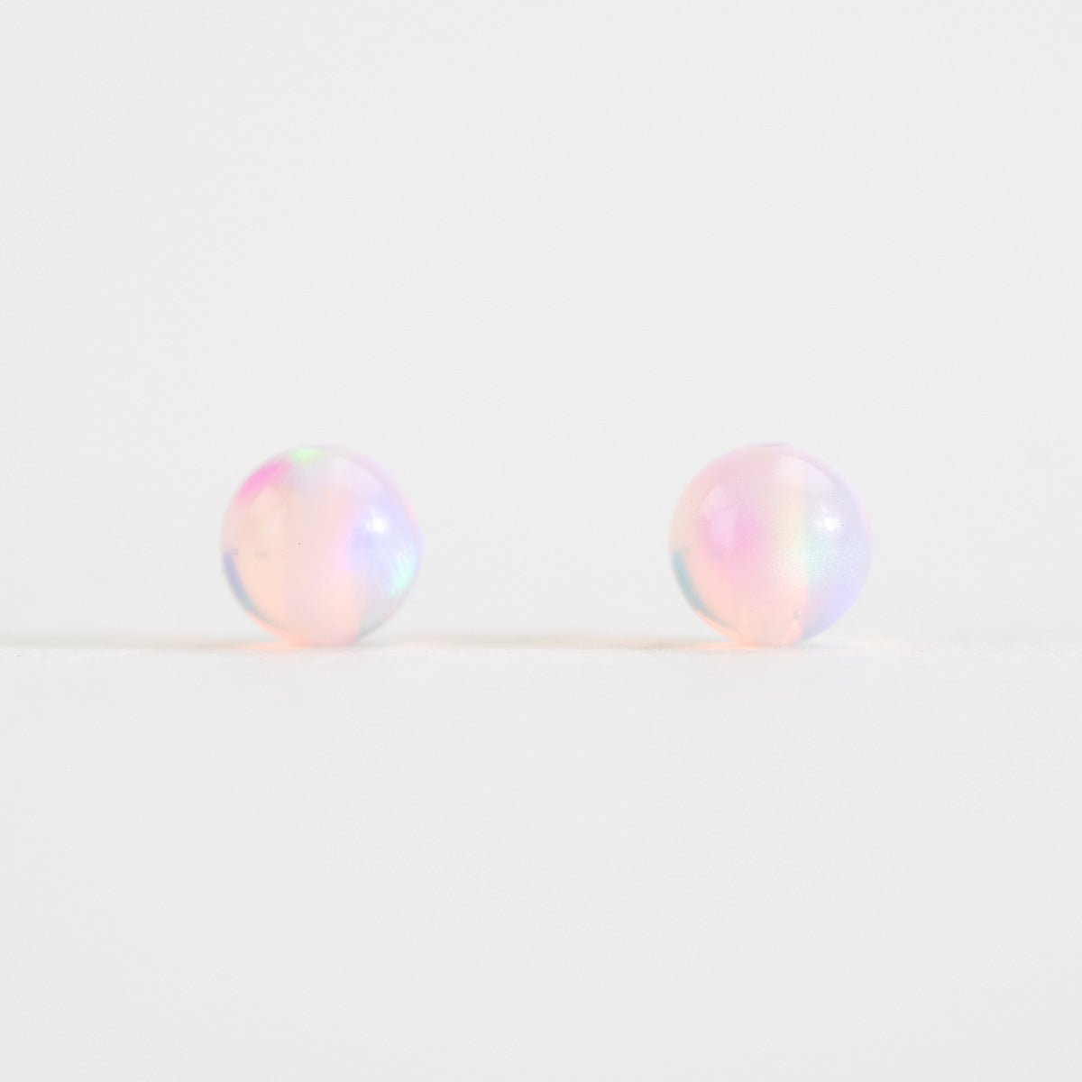 Pair of round, iridescent beads on a light white background