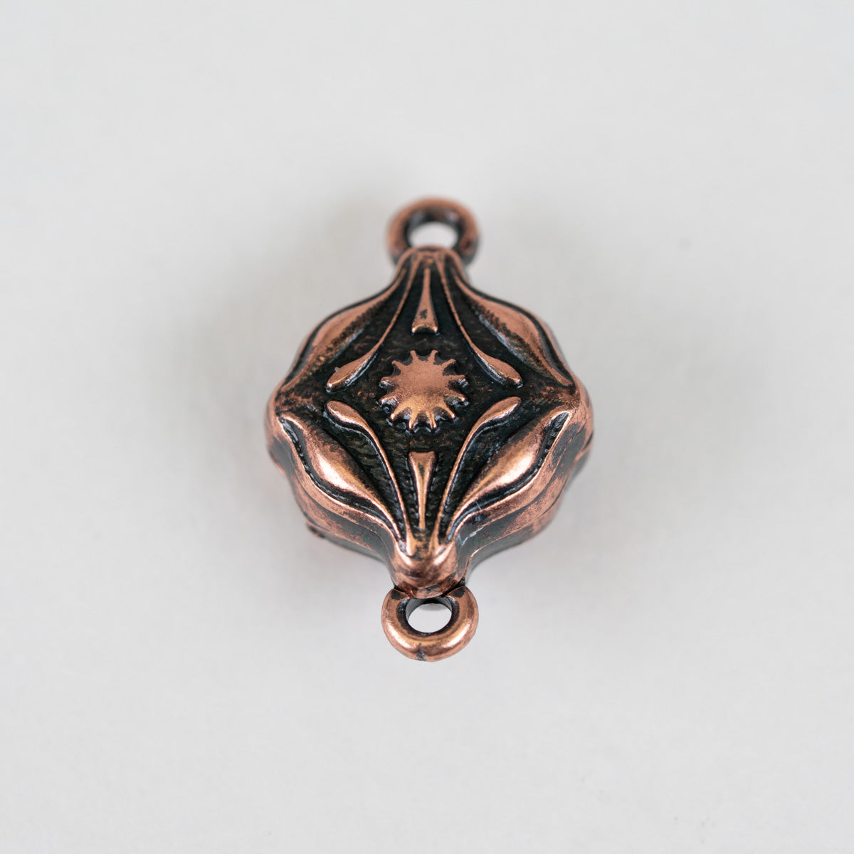 A single decorative metal charm or pendant with a copper-toned finish and dark oxidized recesses, photographed on a plain light background.