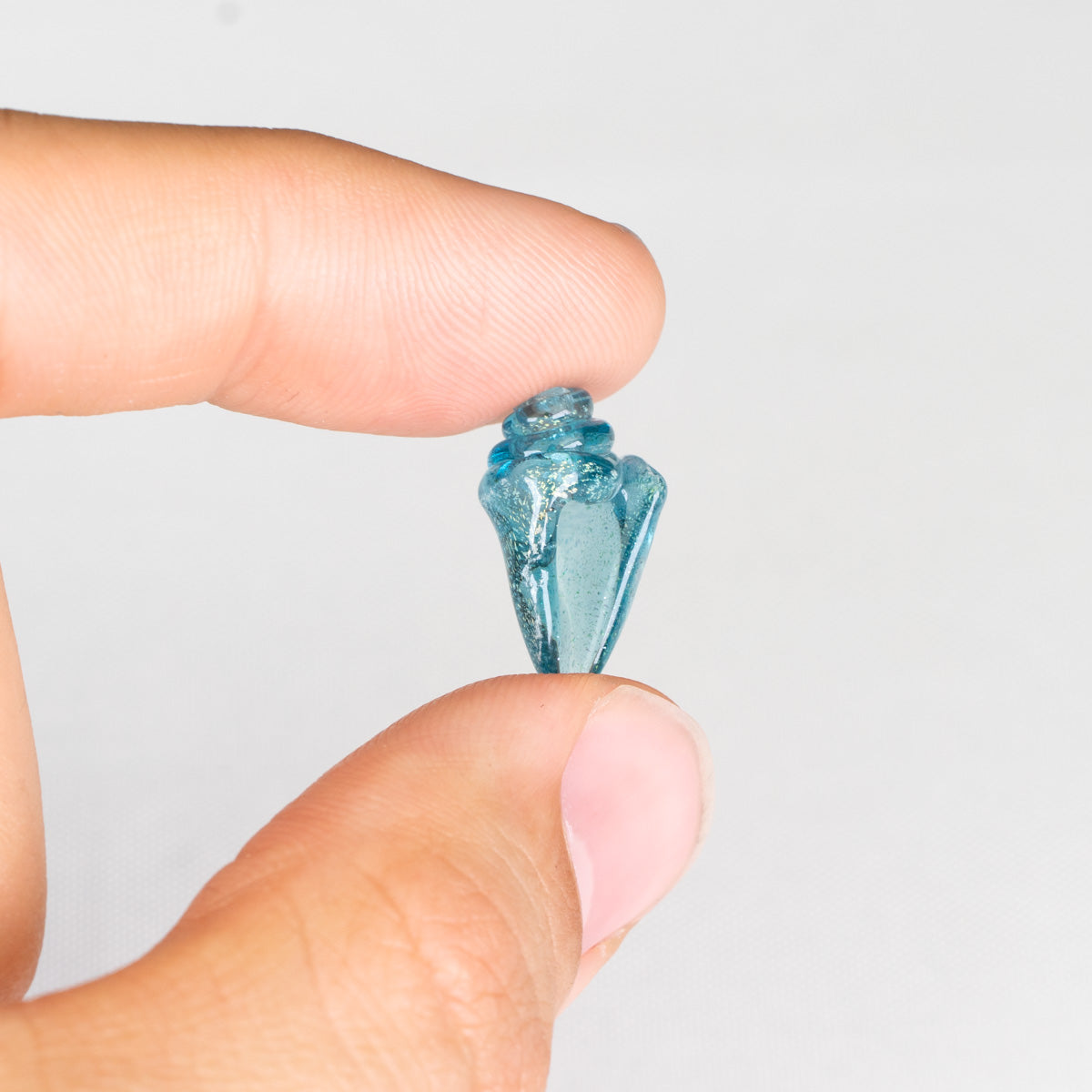 Clear seashell bead held between fingers against a light white background