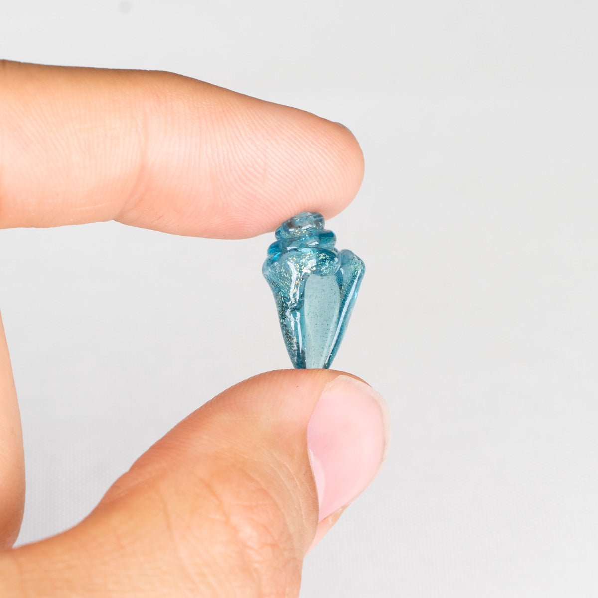Clear seashell bead held between fingers against a light white background