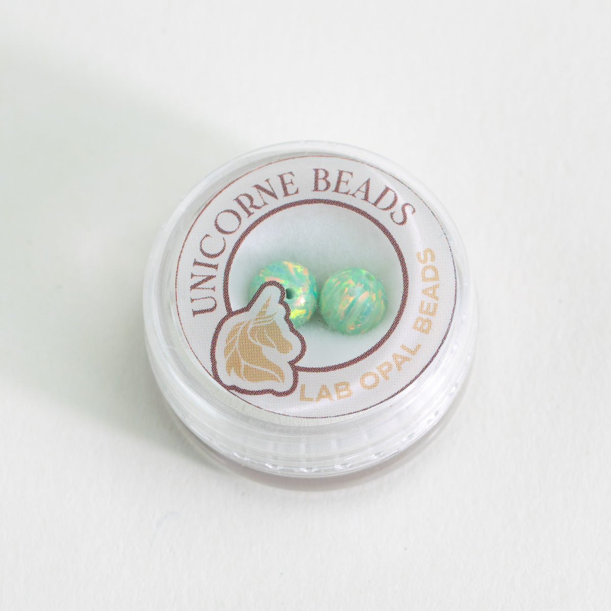 Unicorne Beads container with two green opal beads on a white background