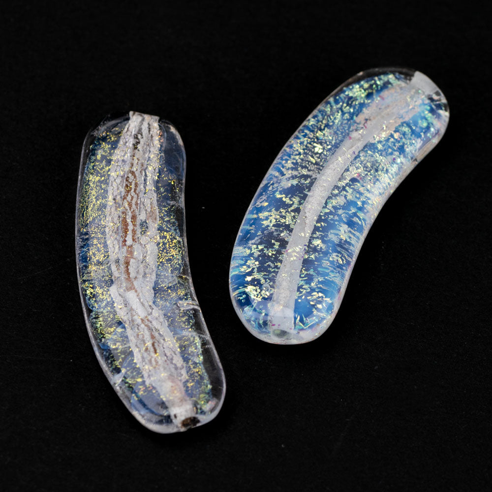 Two Flat Glass beads, shaped with a subtle curve featuring a blue hue with rainbow foil embedded. Each bead has a hollow section running length wise used by jewelry makers to place on a string. 