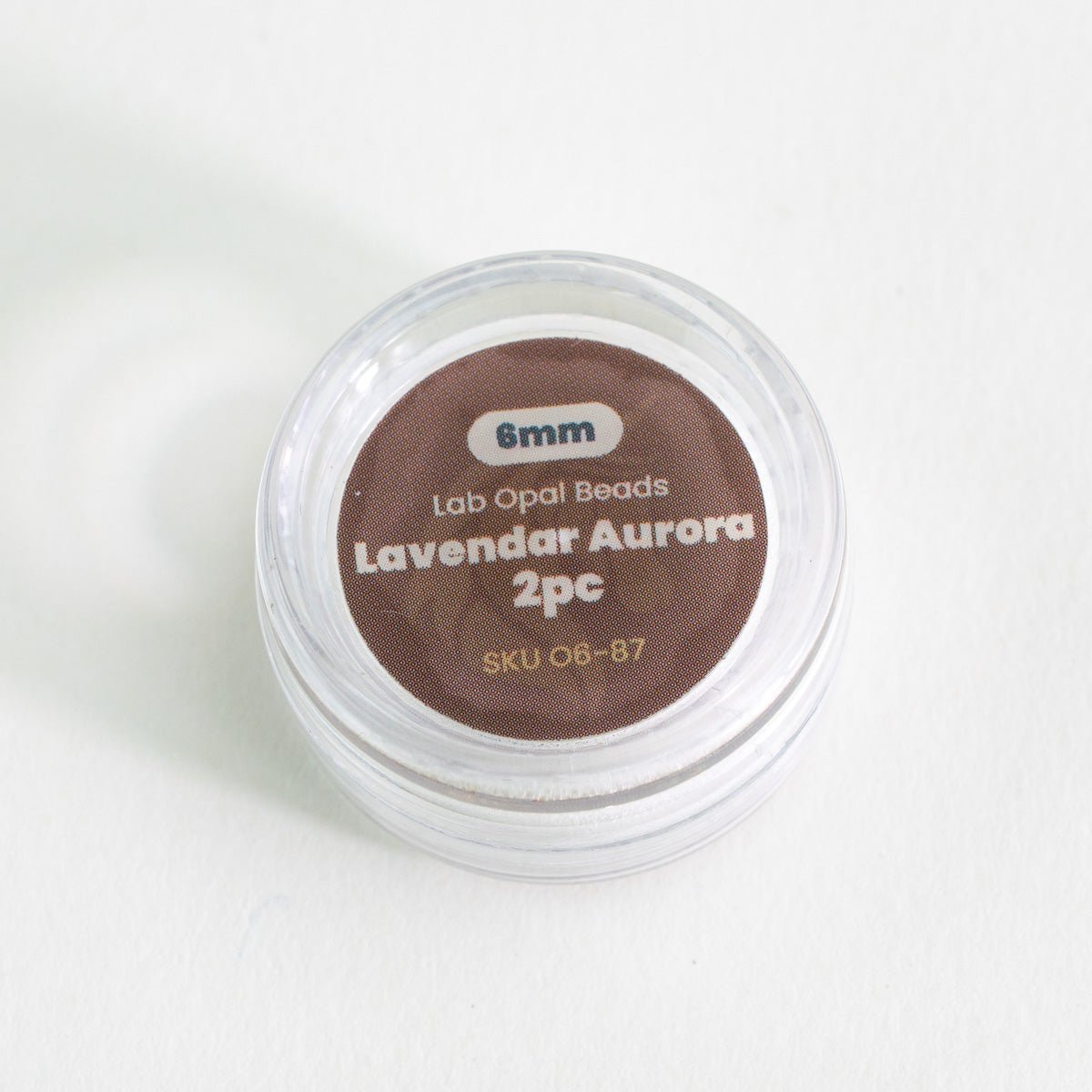 Small container of lavender aurora lab opal beads on a white background