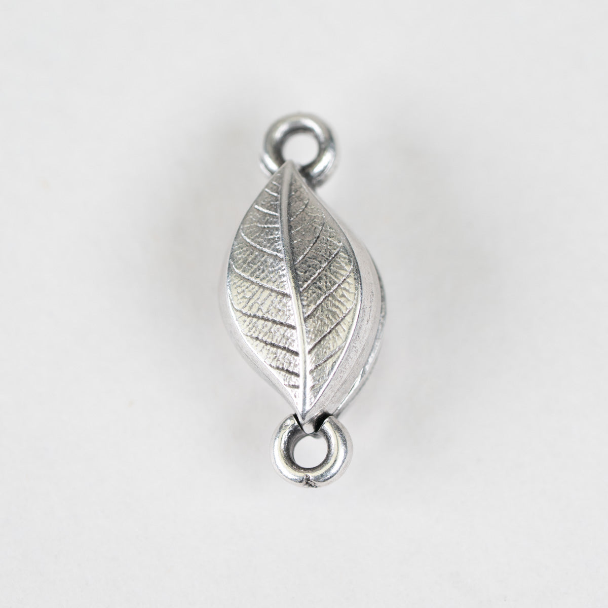 A silver-toned metal leaf-shaped charm with detailed leaf veins and two hanging loops, shown on a plain light gray background.