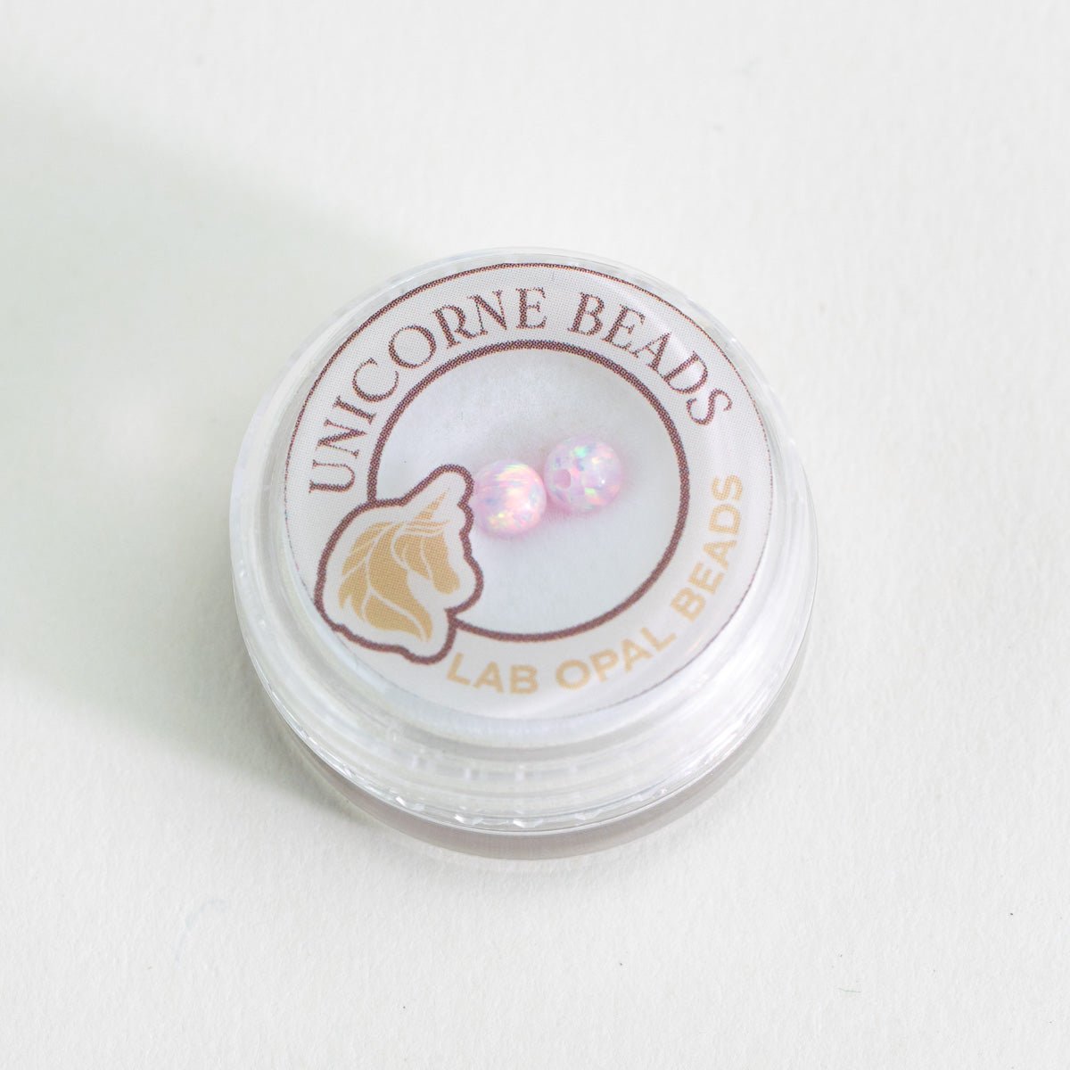 Container of Unicorne Beads with lab opal beads on a white background