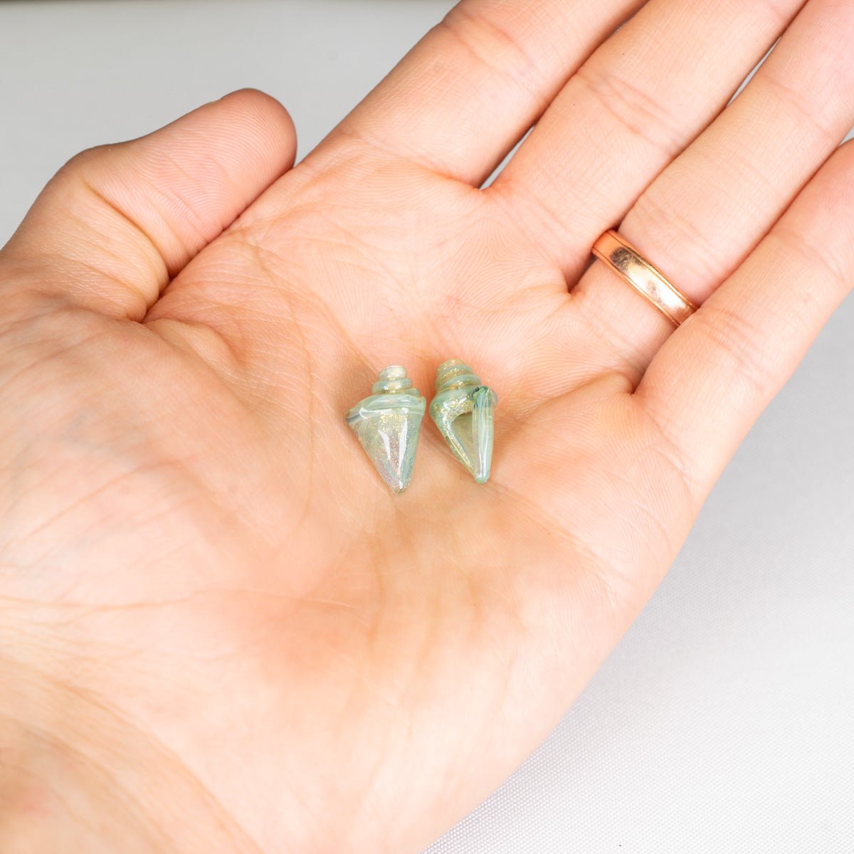 Two small green seashell beads held in a hand against a white background