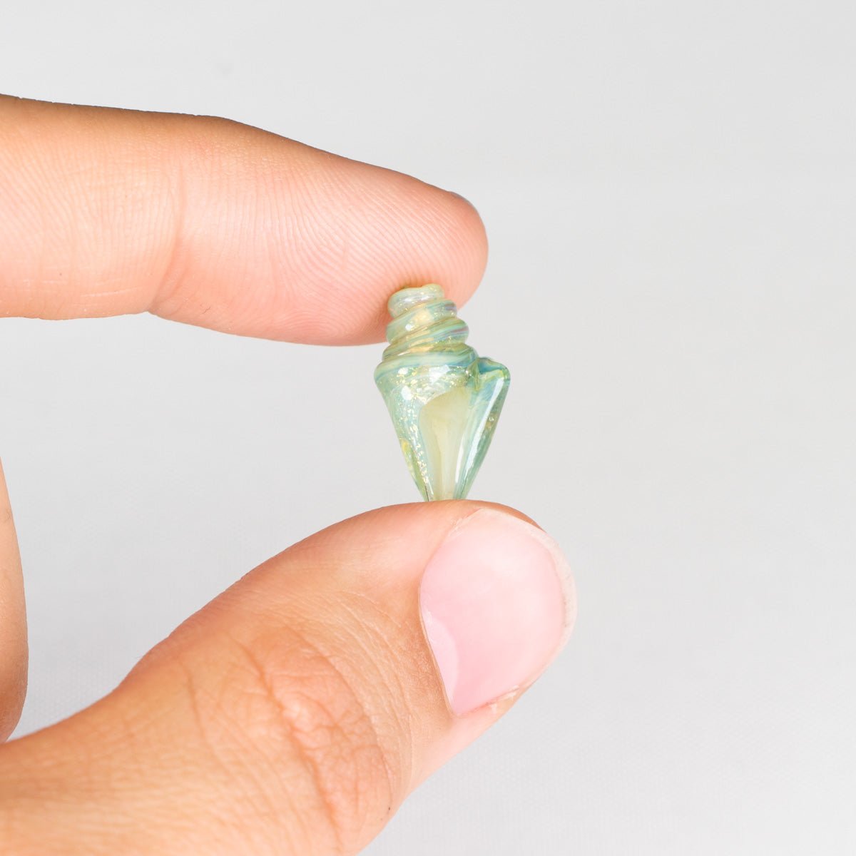 Small green seashell bead held between fingers against a white background