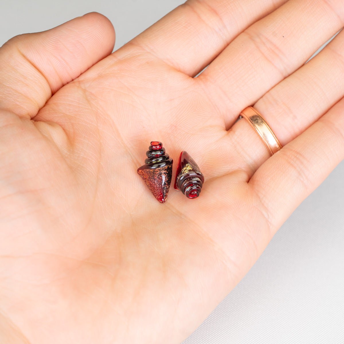 Two small red nobilis seashell beads on a person's palm with a white background
