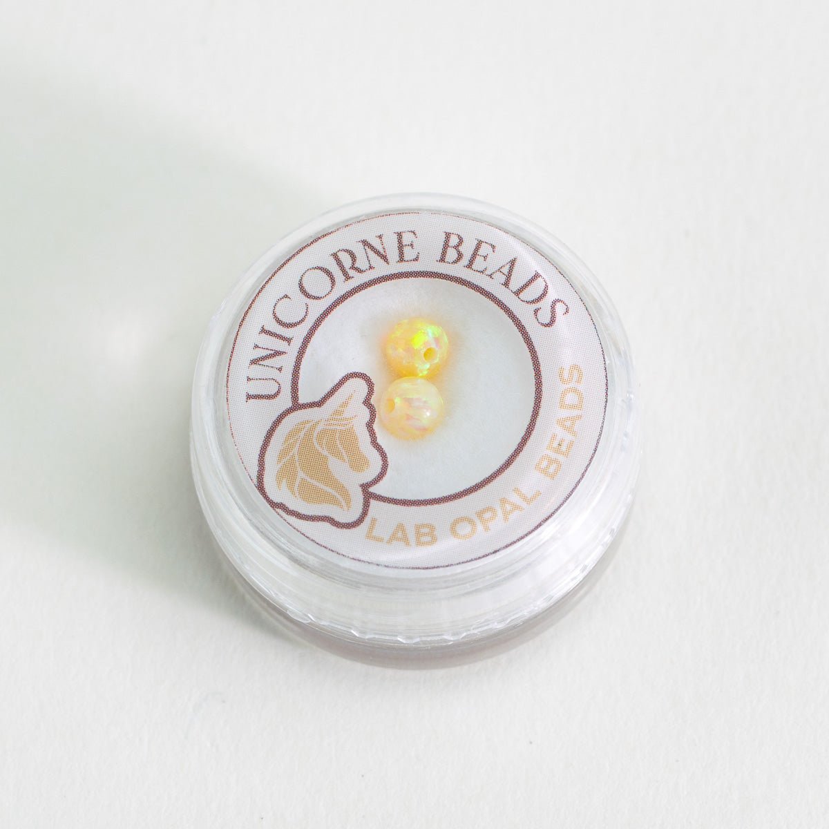 Unicorne Beads container with lab opal beads on a white background