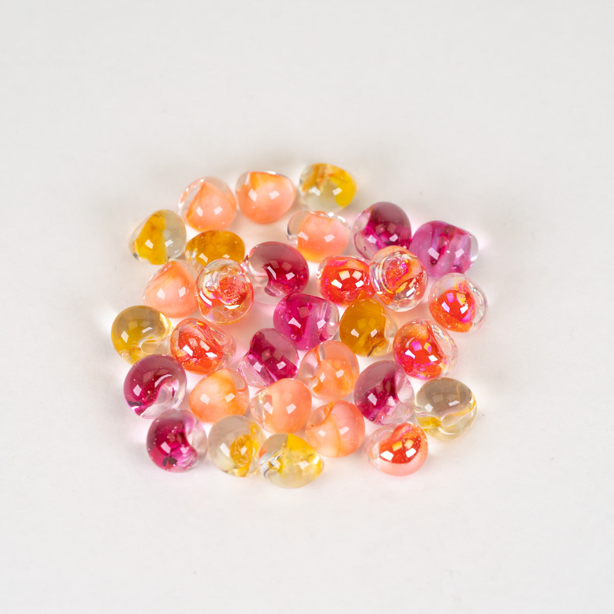 A small pile of colorful, translucent teardrop-shaped beads in shades of pink, orange, yellow, and clear, arranged on a plain white background.