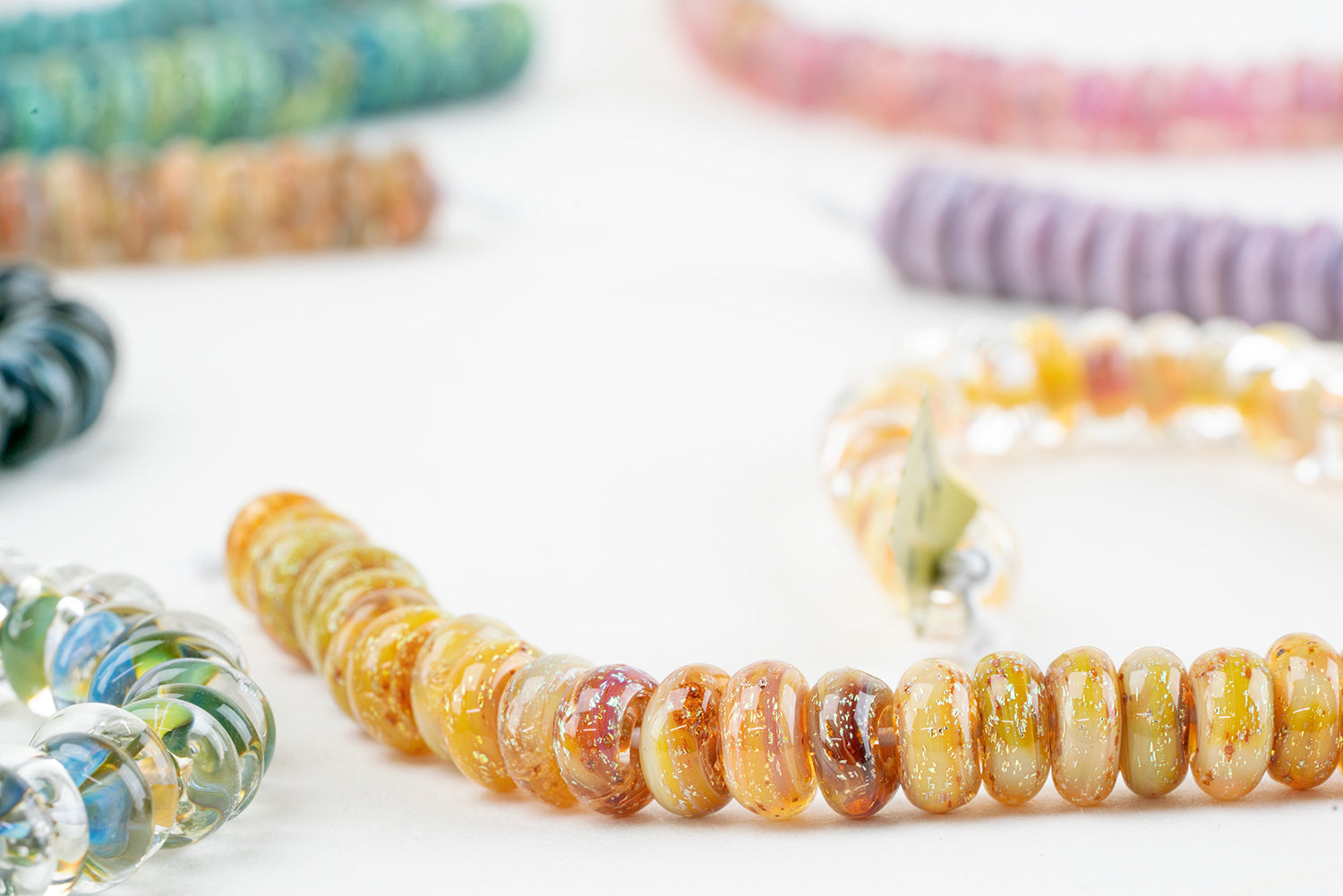 An assortment of different glass beads from Unicorne beads featuring the midnight skies donut bead strand