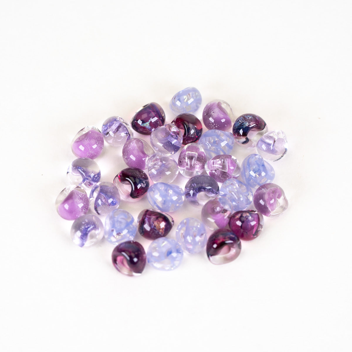 A pile of small, round, faceted glass beads in shades of purple, lavender, and clear with white swirls, arranged on a plain white background.