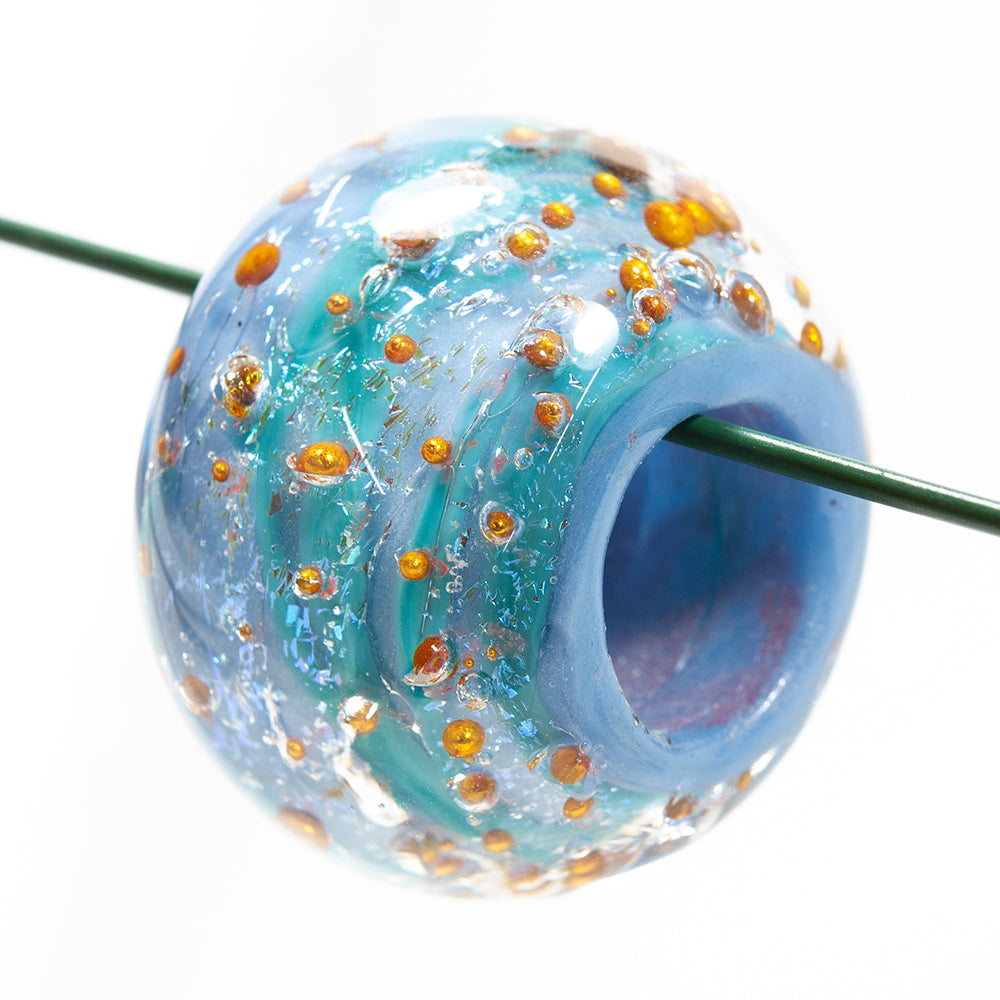 One large glass jewelry bead with blue and purple swirl coloring. The bead has globs of copper beads embedded around the surface of the bead.