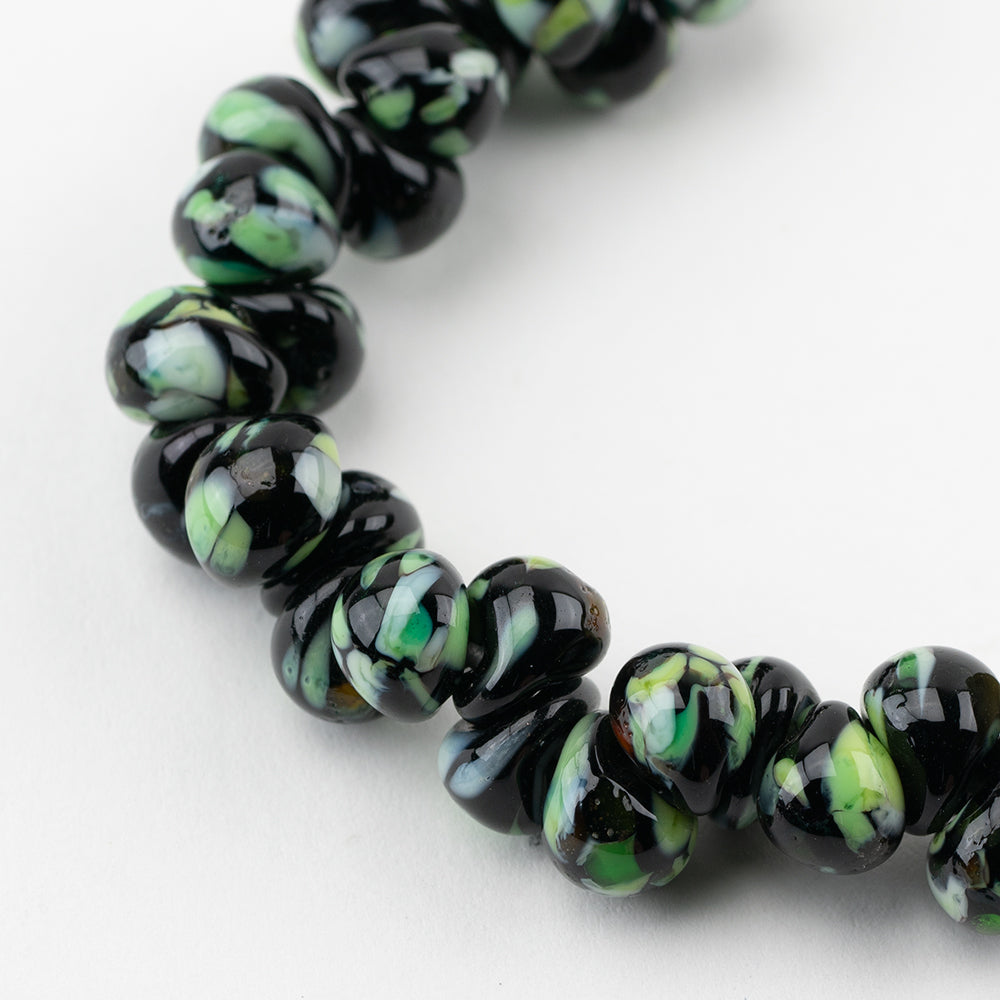 A strand of Geneva Teardrop glass beads crafted by Unicorne Beads. These glass beads are shaped like teardrops and are Black with green accents. Each glass bead has a hole in the middle to be used for jewelry craft projects.