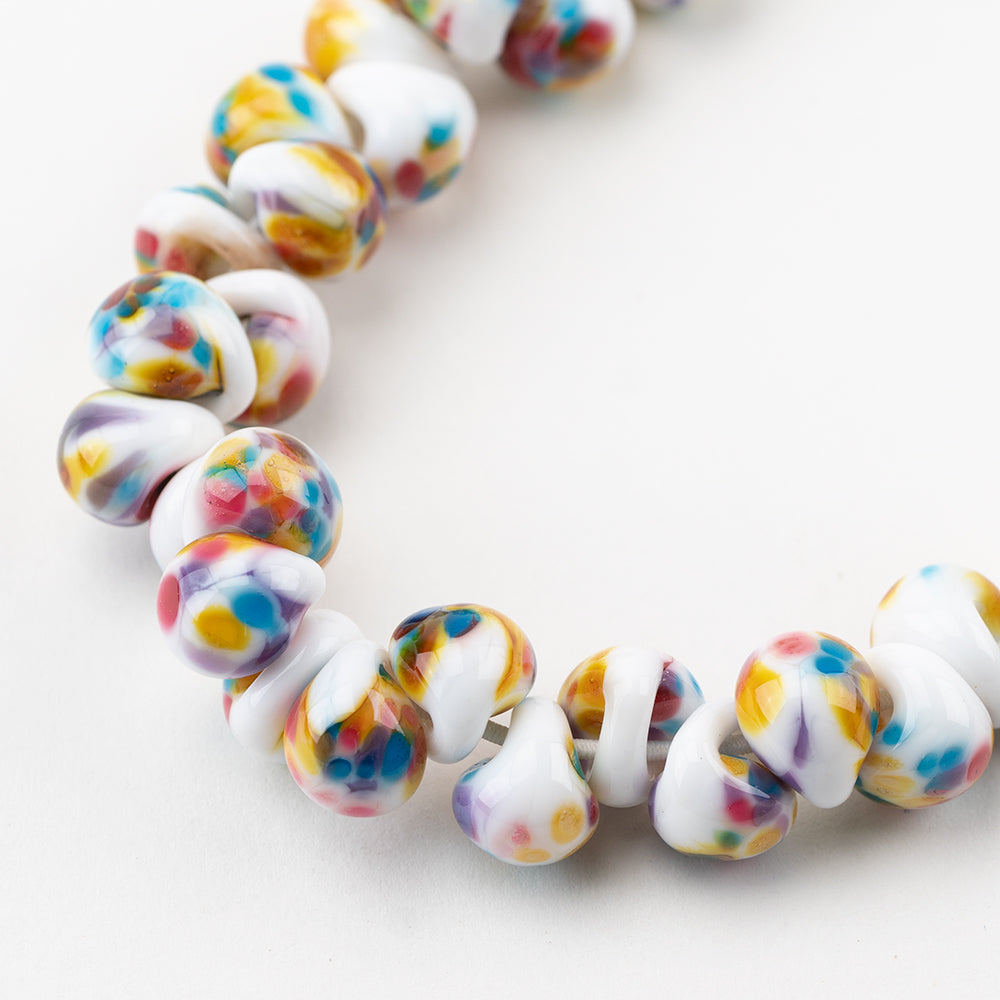 A strand of Aspen Teardrop glass beads crafted by Unicorne Beads. These glass beads are shaped like teardrops and are white with a touch of blue, pink, and orange. Each bead has a hole in the middle to be used for jewelry craft projects.
