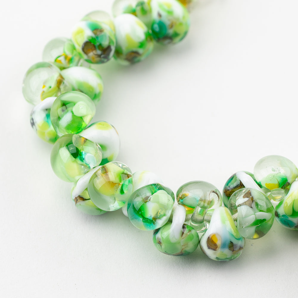 A strand of Key Lime Teardrop beads crafted by Unicorne Beads. These Beads are shaped like teardrops and are green, white, and clear with blue accent swirls. Each bead has a hole in the middle to be used for jewelry craft projects.