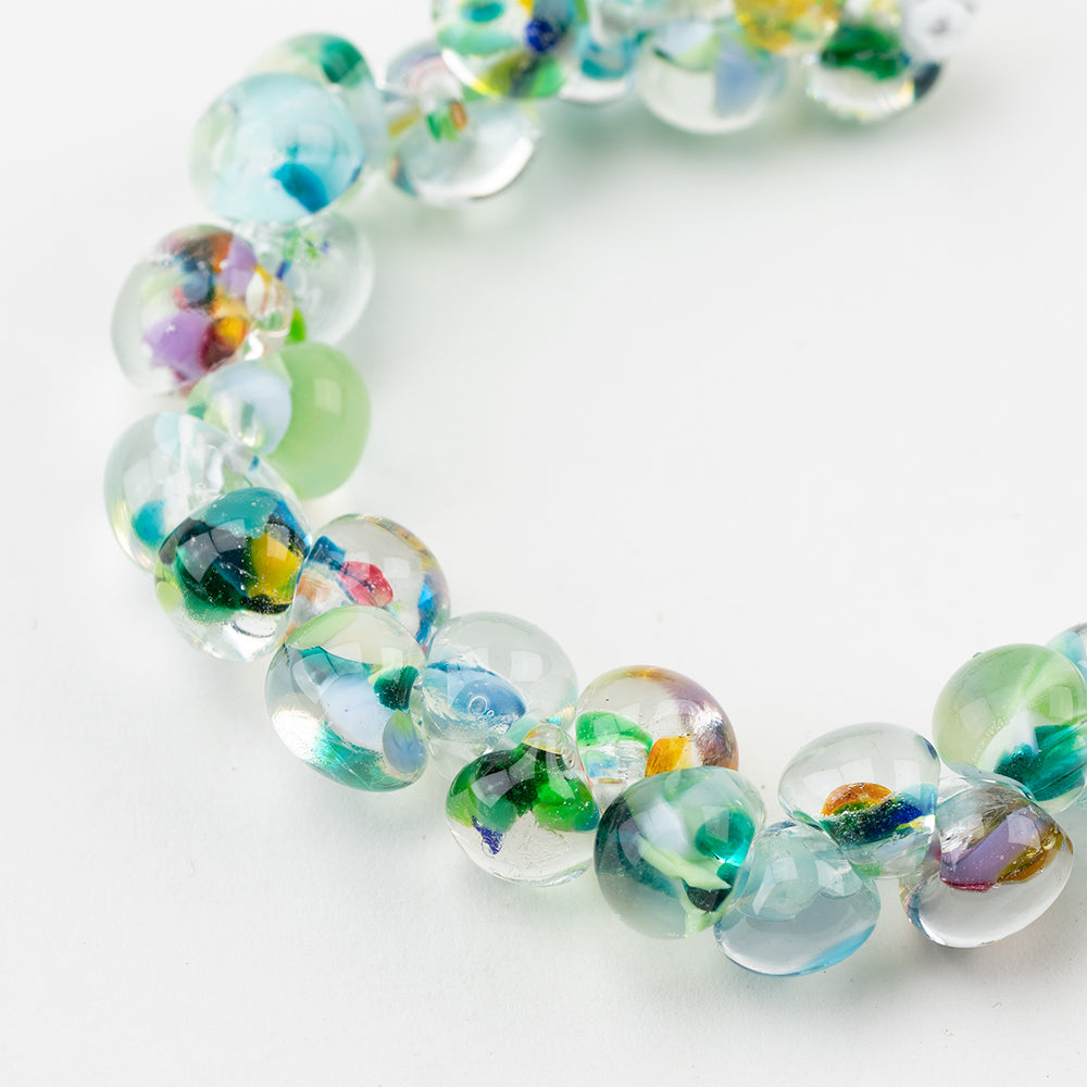 A strand of Monet Teardrop glass beads crafted by Unicorne Beads. These glass beads are shaped like teardrops and are multi-colored. Each glass bead has a hole in the middle to be used for jewelry craft projects.