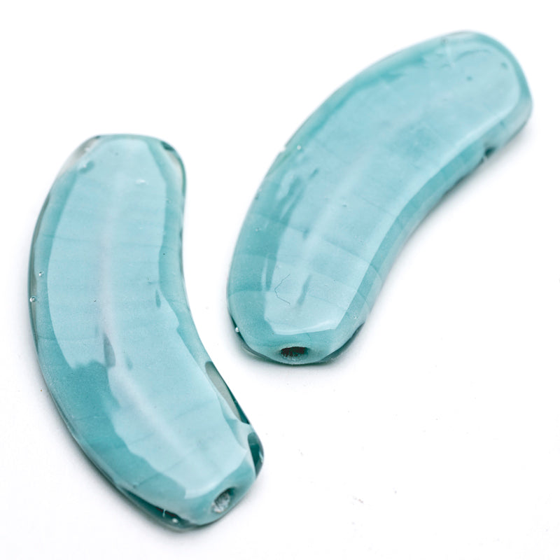Two light-blue banana shaped glass beads with holes in each side meant for jewelry makers to string  through. 