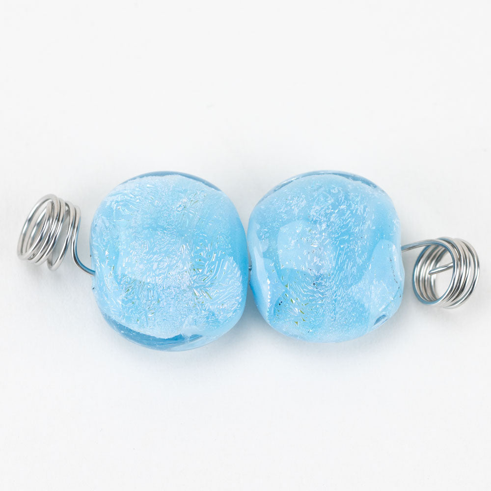 Two glass beads made by Unicorne Beads. Each bead is light blue with dichroic foiling. Each bead has a hollow center to be used for making jewelry artworks.