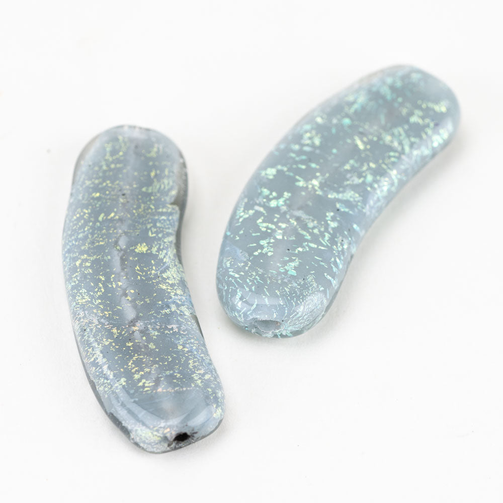 A pair of two banana shaped glass beads from Unicorne Beads. Each bead features a main white, snowy color with hints of colored dichroic foil embedded in the bead. Each bead has two holes on each used by craft makers and jewelry makers to place on a string. 