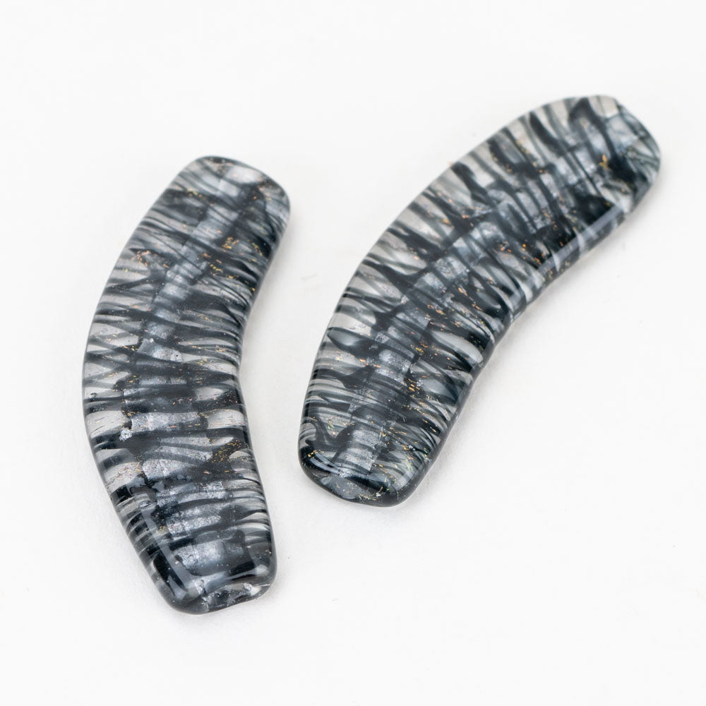 A set of two banana shaped glass beads with black and clear alternating color scheme. Each bead has a hole on each side, lengthwise, that runs through the entirety of the bead. 