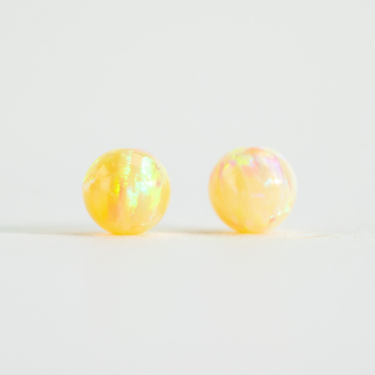 Pair of yellow opal stud beads on a light white background