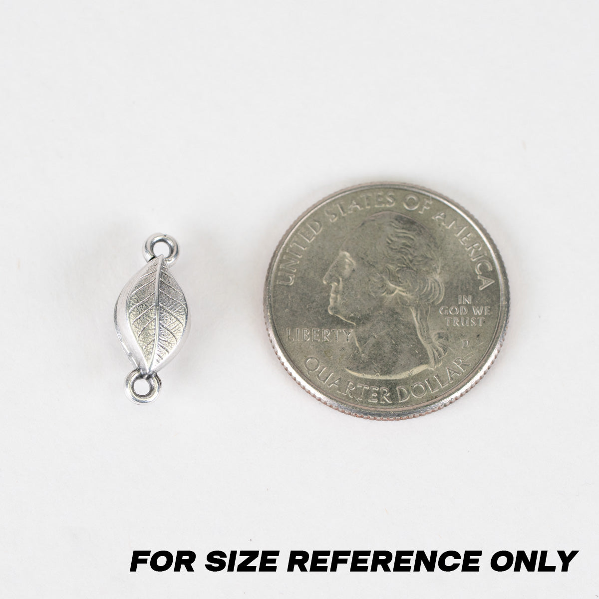 A small silver leaf-shaped bead or charm shown next to a U.S. quarter