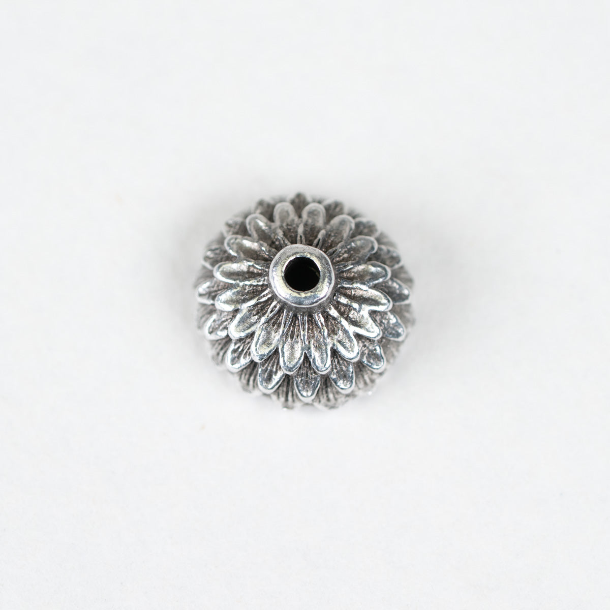 A single silver-toned metal flower-shaped bead with a textured petal pattern and a central hole, shown on a plain white background.