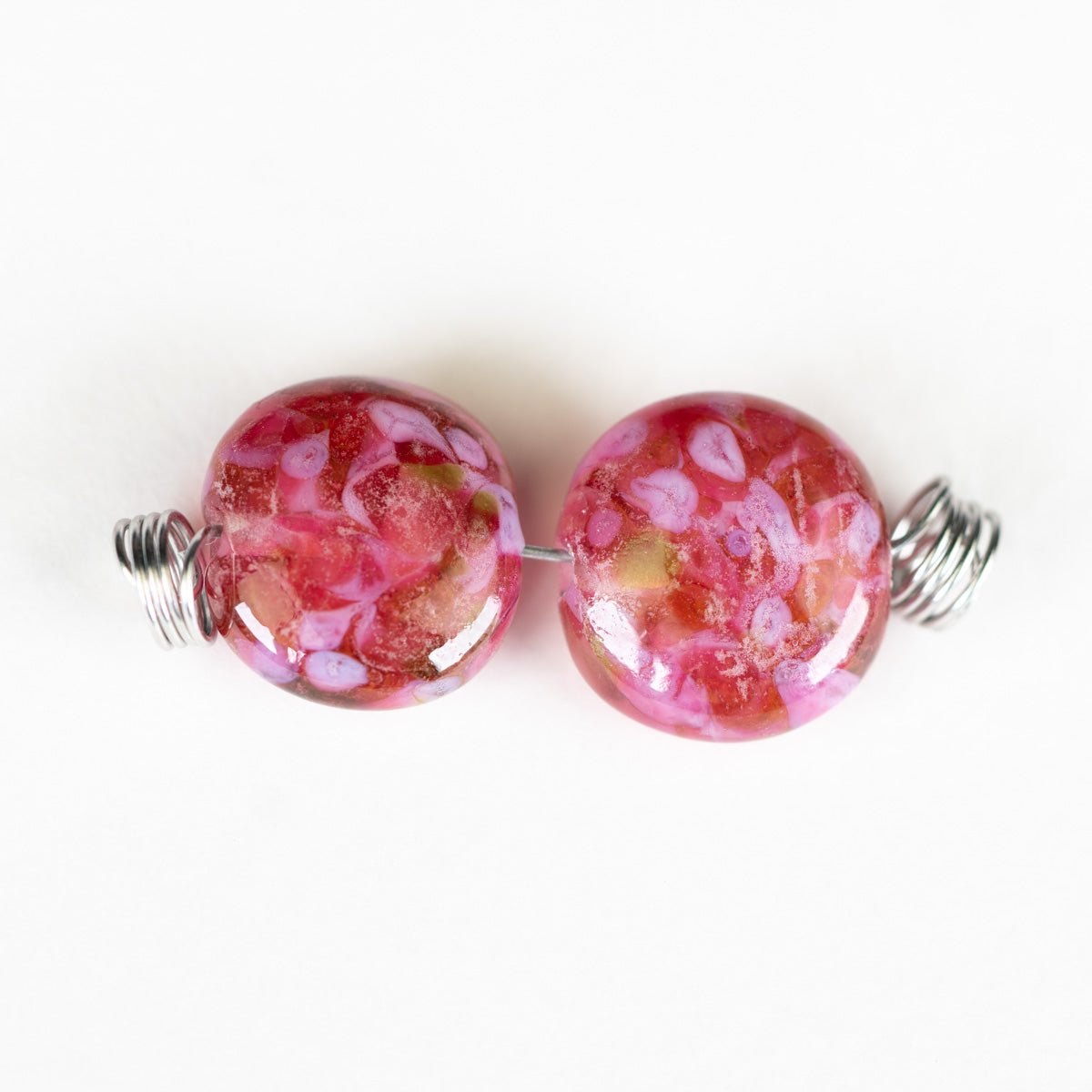 Pair of pink glass beads with silver wire loops on a white background