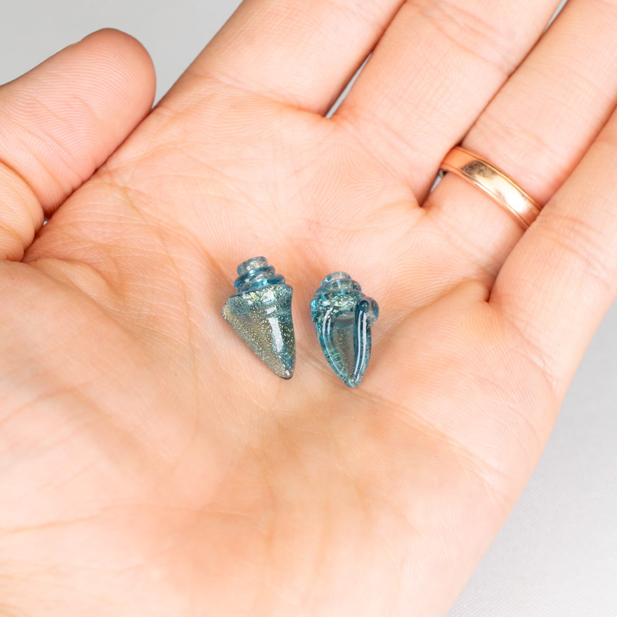 Blue conch shell beads held in a hand with a white background
