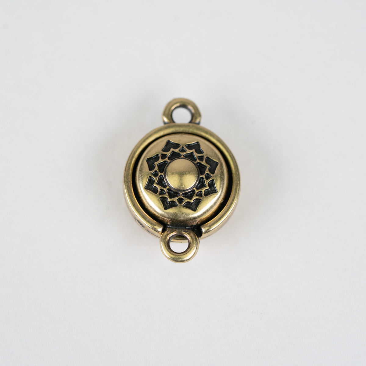An antique bronze metal charm with a circular design, featuring a central lotus flower motif and two hanging loops, shown on a plain white background.