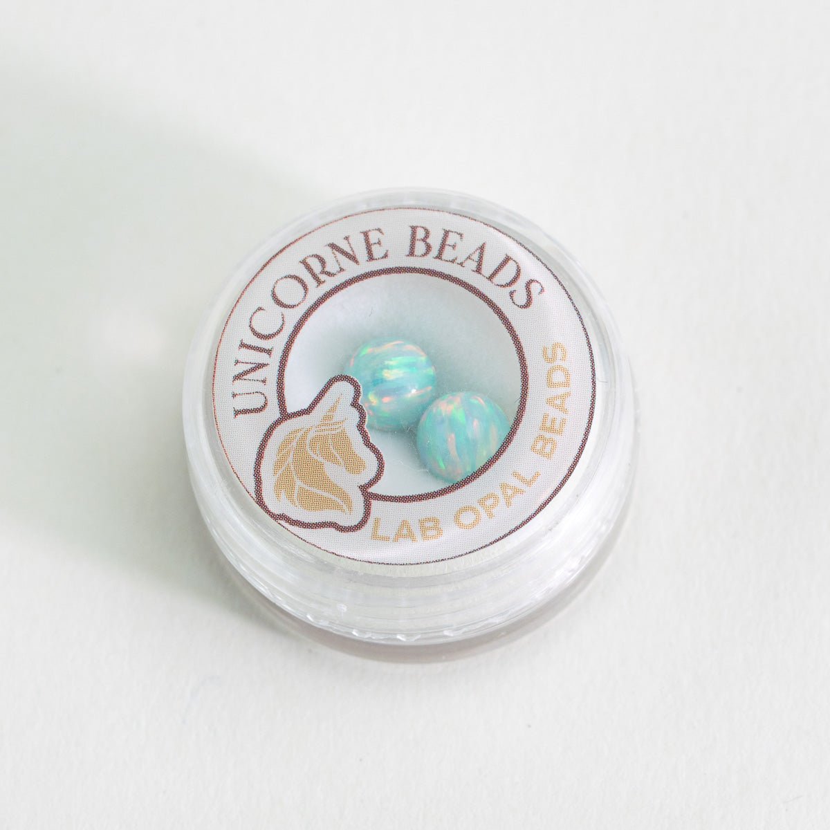 Container of Unicorne Beads with two lab opal beads on a white background