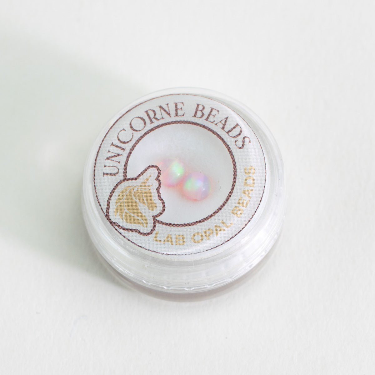 Container of Unicorne Beads with two lab opal bead on a white background