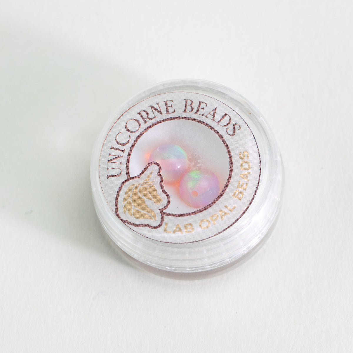 Container of Unicorne Beads with lab opal beads on a white background
