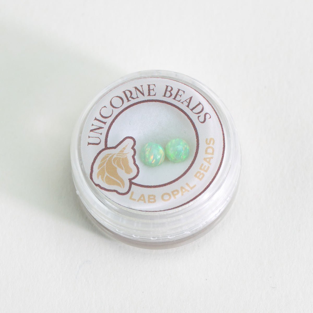 Unicorne Beads container with two green lab opal beads on a white background