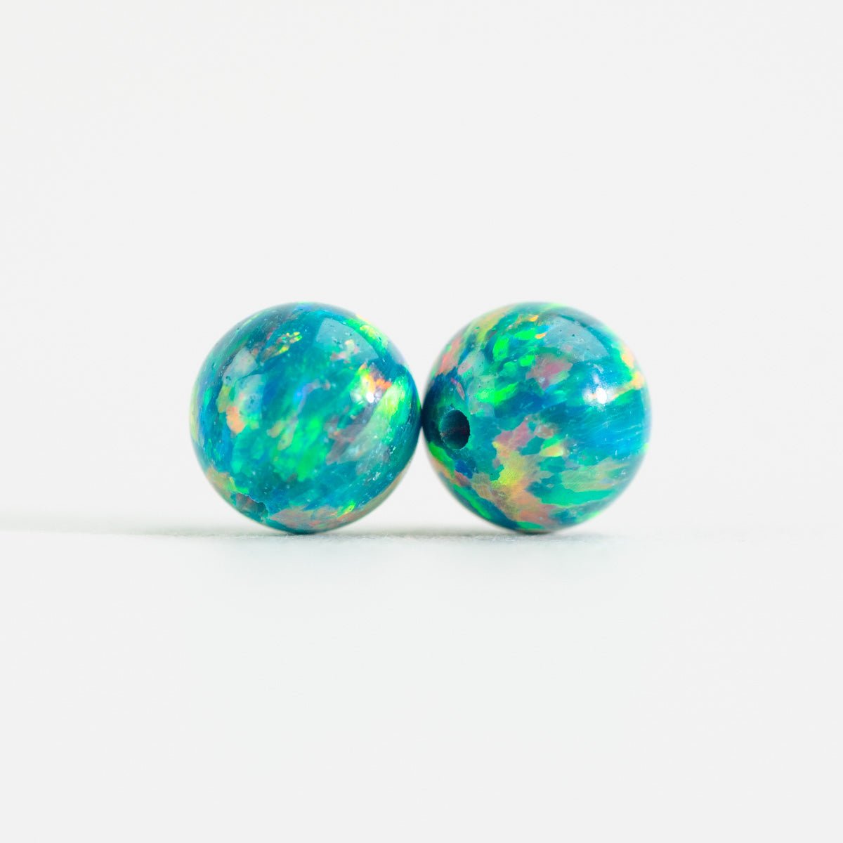 Two opal beads with a multicolored pattern on a white background