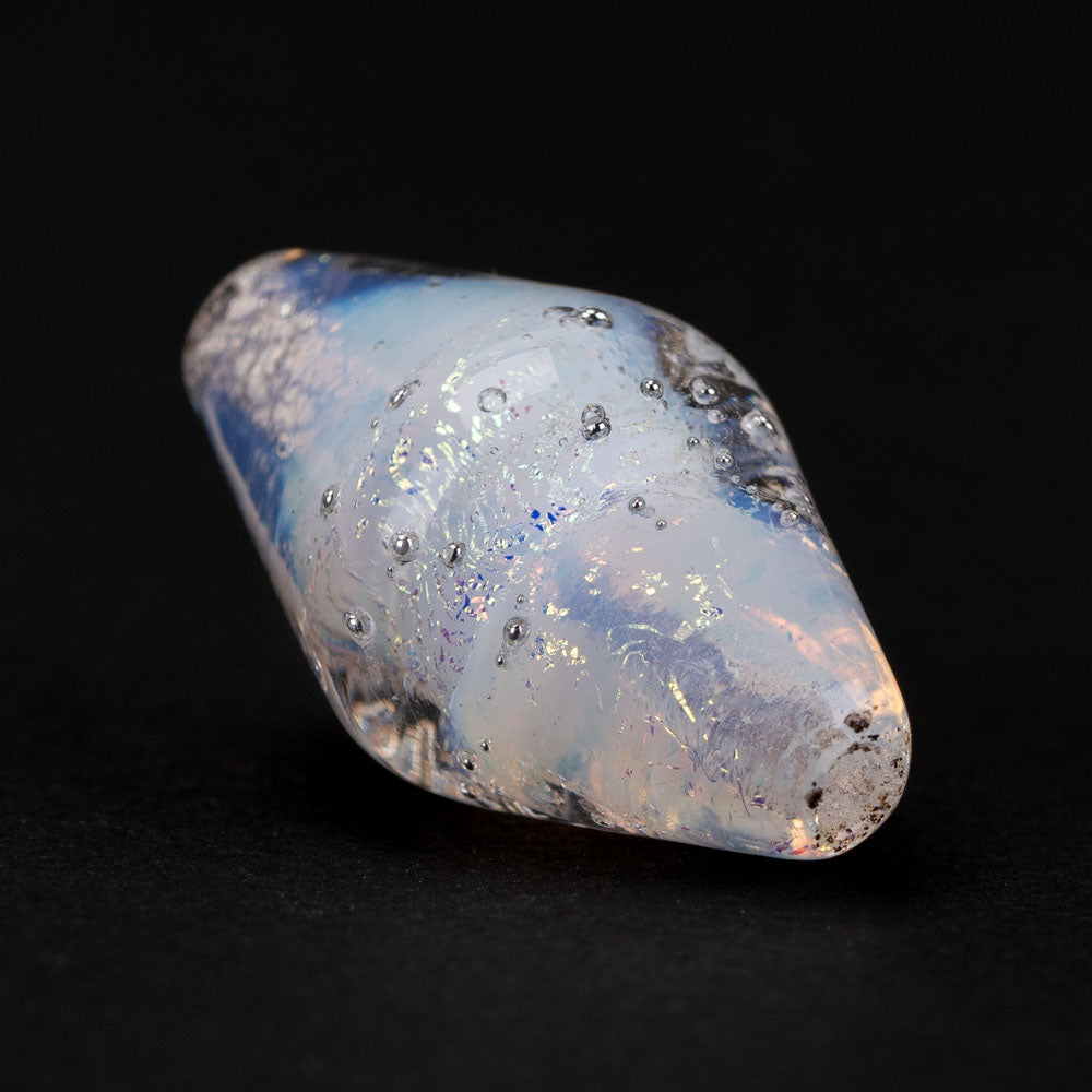 Clear glass bead with a blue and purple hue sitting on a black back drop. Bead has drops of silver embedded in the outer shell and include two holes use for necklace making. 