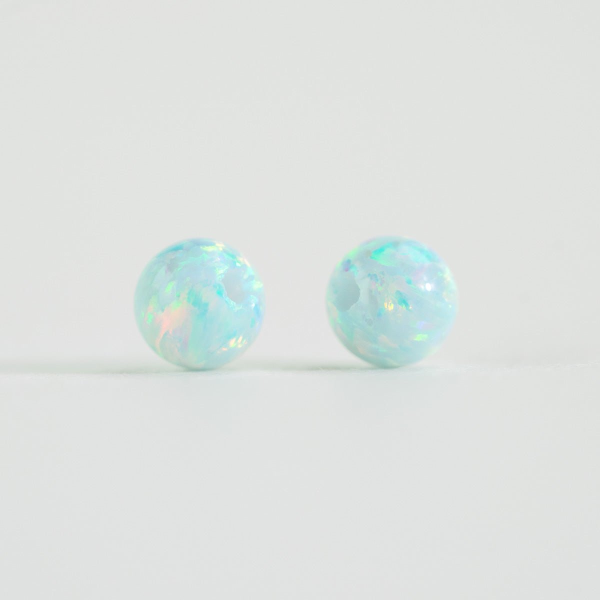 Pair of opal blue stud beads on a light white background