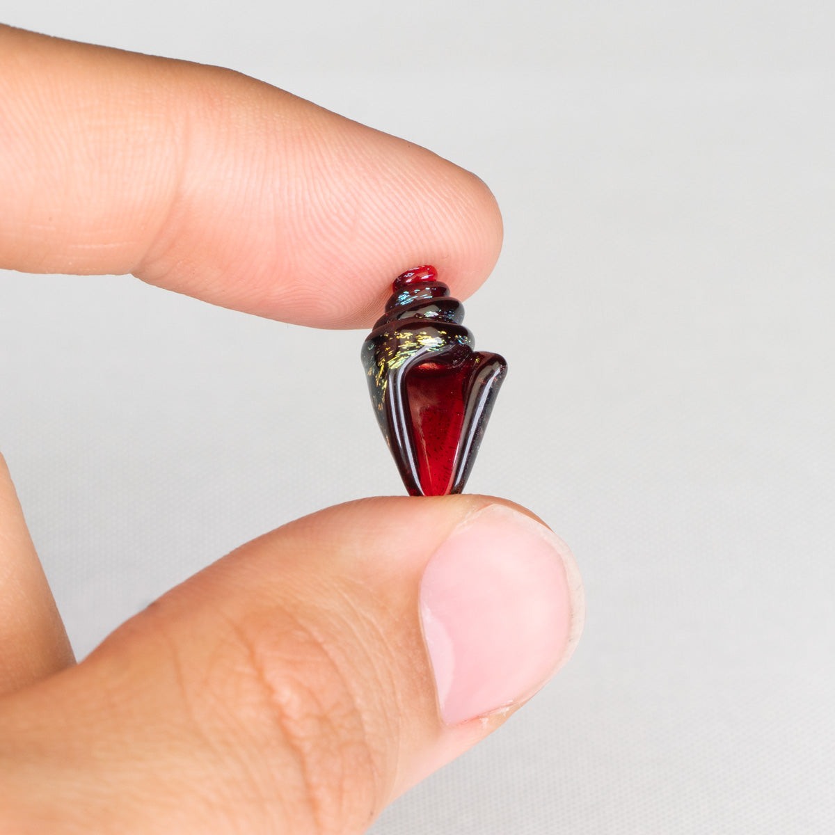 Hand holding a red and black glass bead against a white background