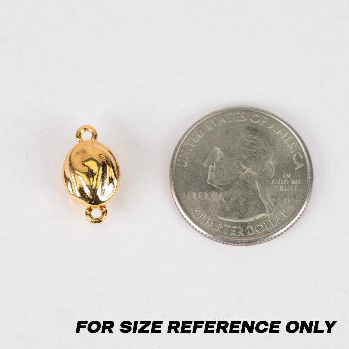 A small polished gold oval bead or charm shown next to a U.S. quarter