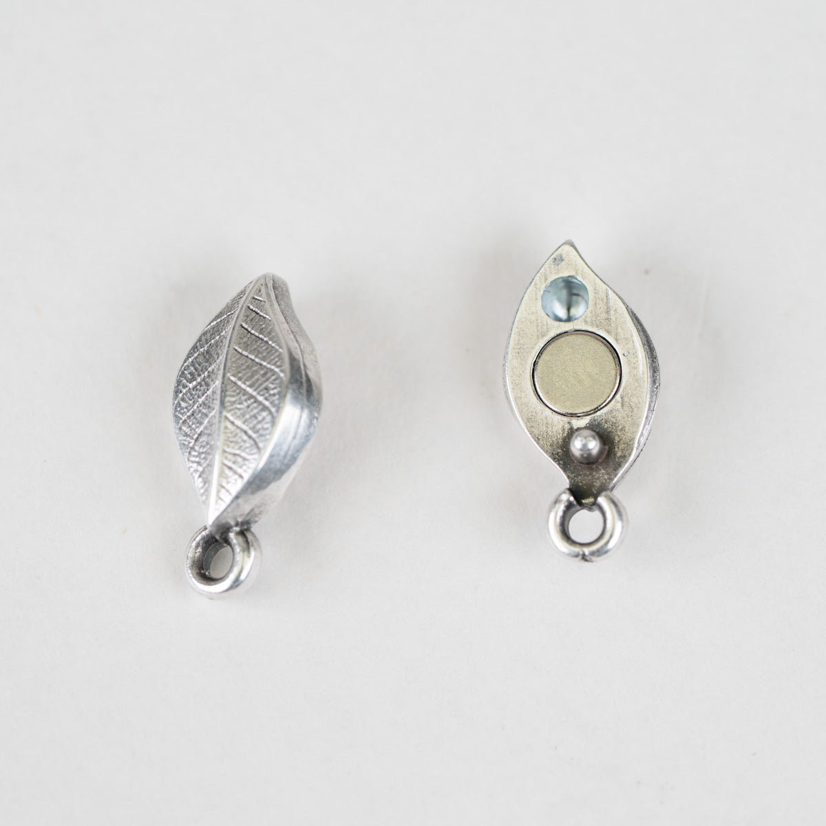 Two silver-toned metal leaf-shaped jewelry findings with hanging loops, shown on a plain light background.
