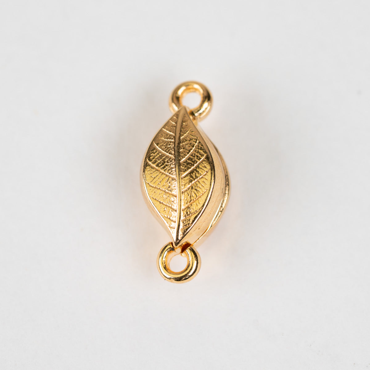 A gold leaf-shaped charm with detailed leaf veins and two hanging loops, shown on a plain white background.