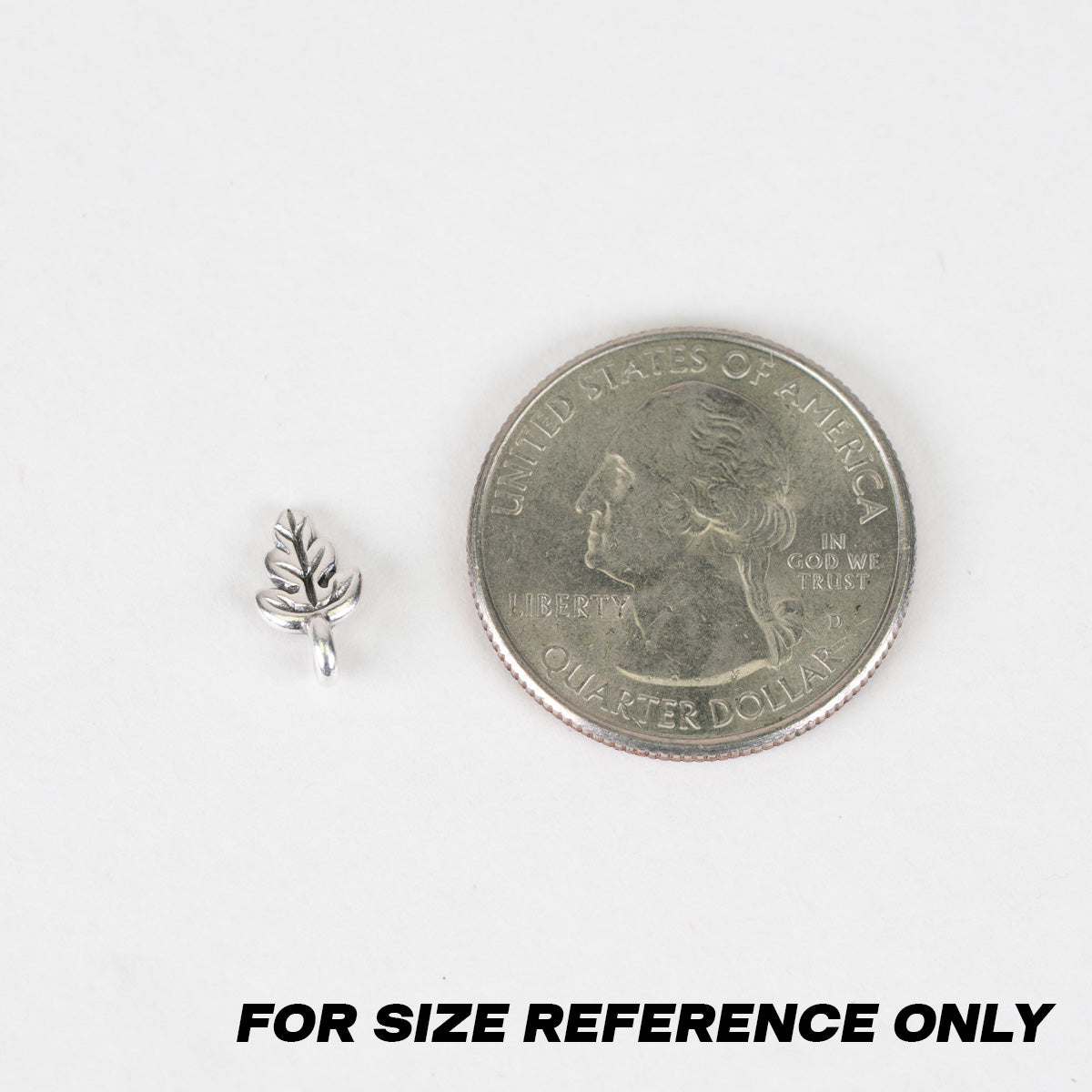 A small silver leaf-shaped charm or bead shown next to a U.S. quarter