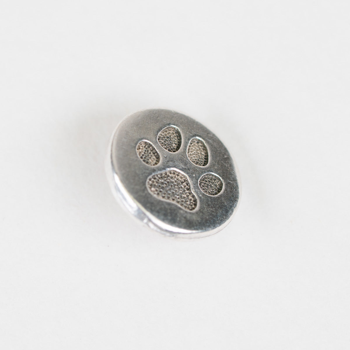 A round silver metal charm featuring an embossed paw print design, shown on a plain white background.