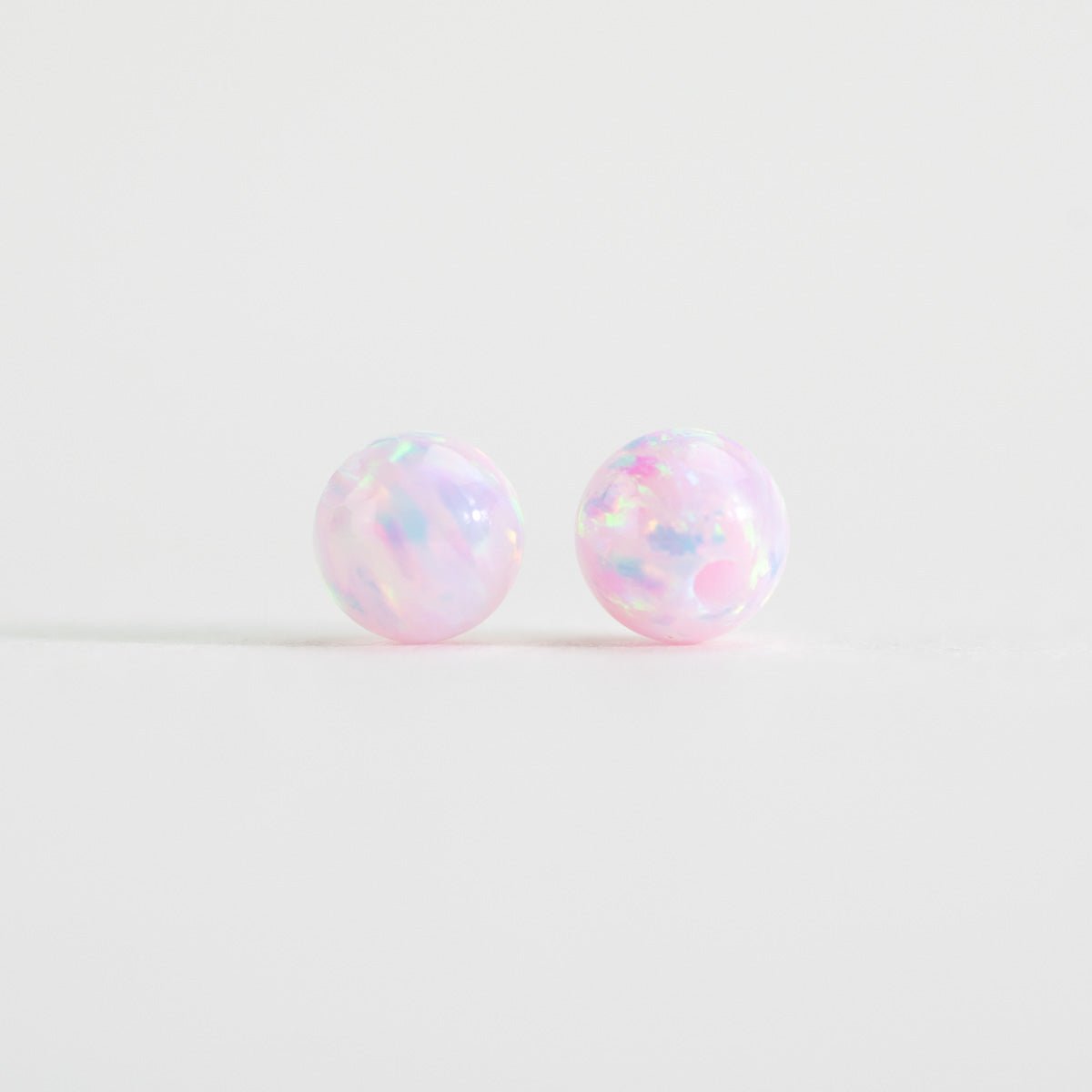 Pair of iridescent round pink beads on a light white background