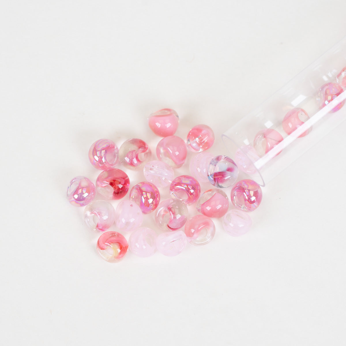 Mini pink glass teardrop beads scattered on plain white background