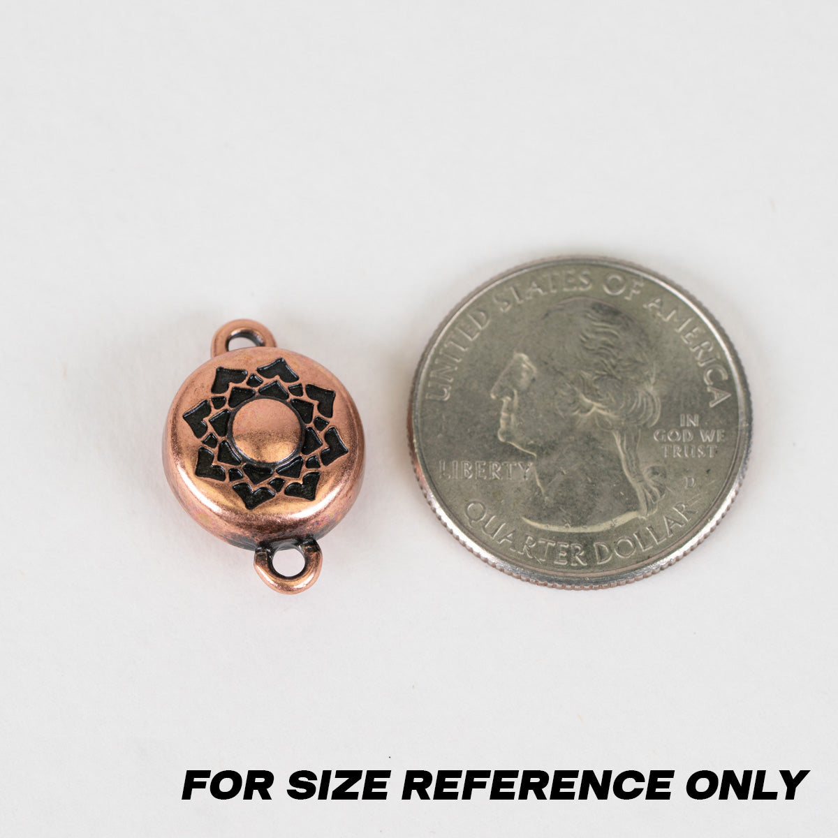 A small round copper-toned bead or charm with black enamel detailing, shown next to a U.S. quarter