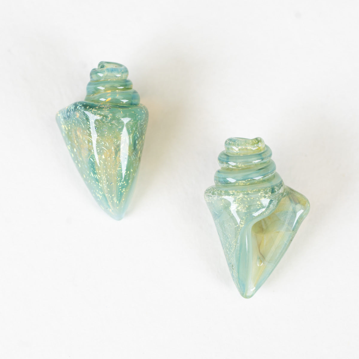 Two green glass seashell beads with a textured surface on a white background