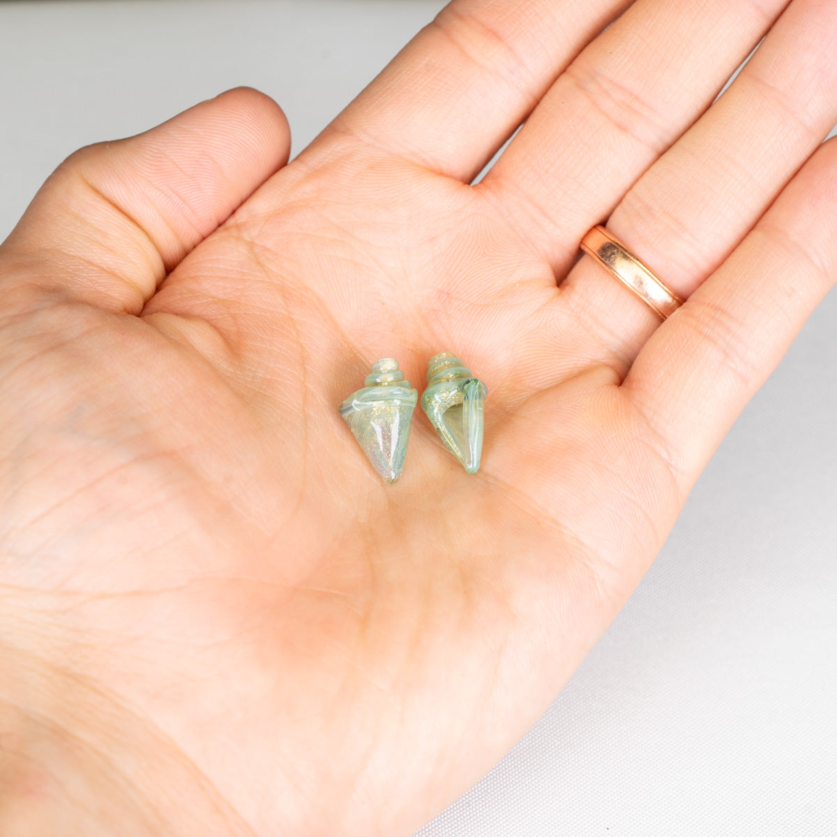 Two small green seashell beads held in a hand against a white background