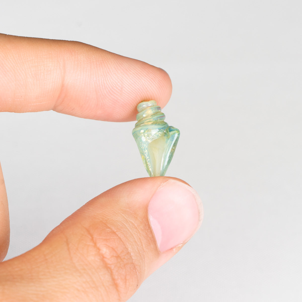 Small green seashell bead held between fingers against a white background